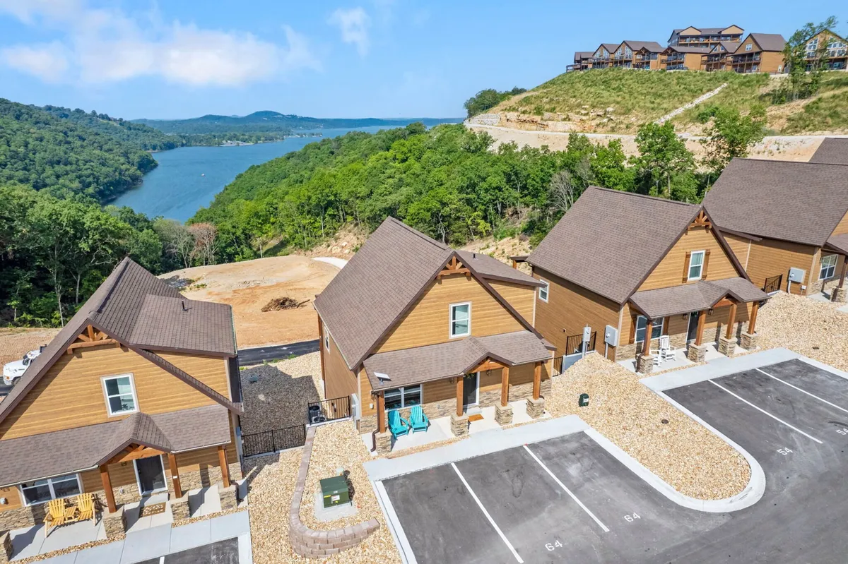 An exterior view of charming wooden cabins surrounded by lush greenery, with a serene lake visible in the background. The tranquil setting is enhanced by an inviting porch and ample outdoor space, ideal for relaxation and family gatherings.