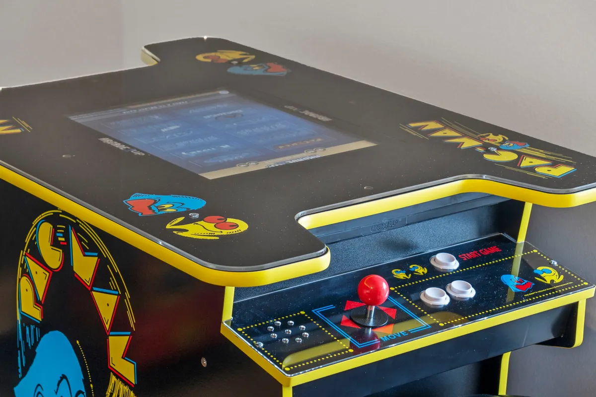 This image features a vibrant interior scene with a classic Pac-Man arcade machine at the center, surrounded by colorful graphics and a detailed control panel. The setting is lively and playful, suggesting a space dedicated to fun and friendly competition.