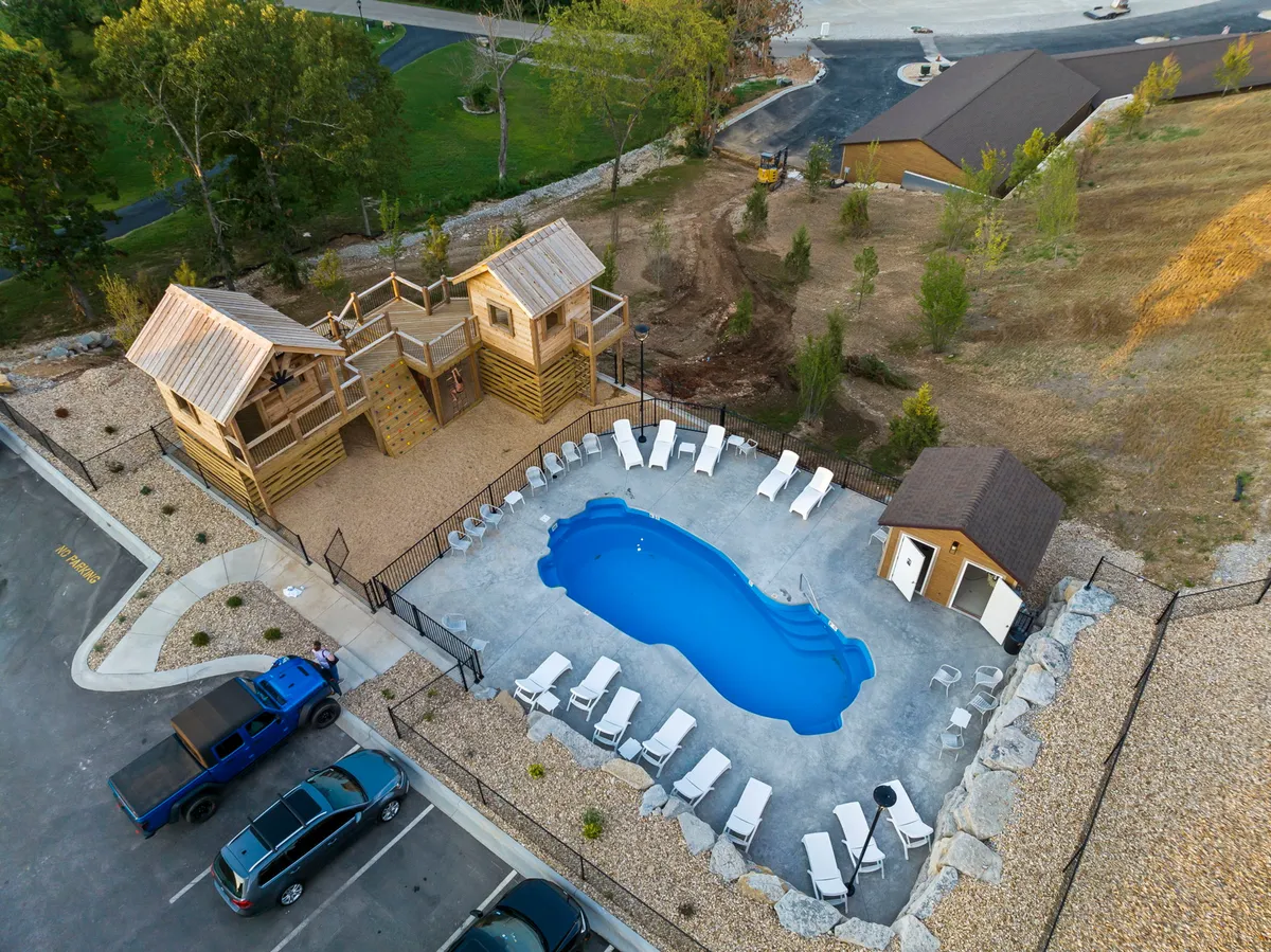 This vibrant exterior image shows a sparkling swimming pool surrounded by lounge chairs and beautifully landscaped grounds. A wooden play structure, perfect for children, sits adjacent to the pool, while families and kids are seen enjoying both the pool and the play area. The scene exudes a lively, inviting atmosphere, ideal for multigenerational fun and outdoor gatherings.