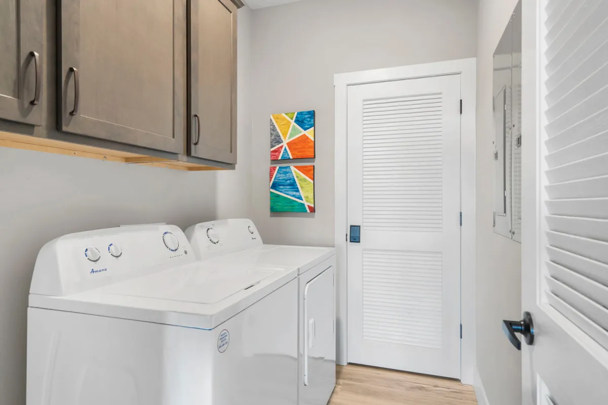 A practical, organized laundry area with a washing machine, colorful artwork, and cabinets for supplies. The space feels clean and well-maintained, highlighting the availability of private laundry facilities.