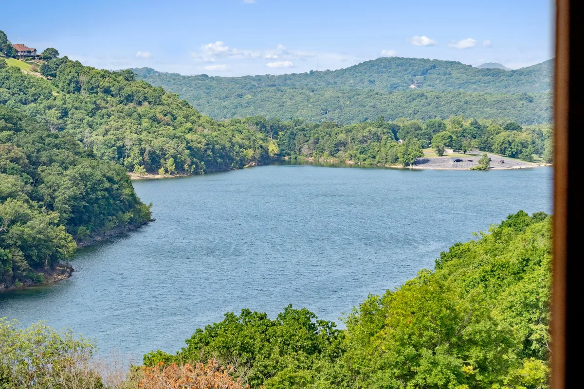 A breathtaking panoramic view of Table Rock Lake, framed by trees and mountains in the distance. The tranquil scene includes the shimmering lake water, ideal for fishing, boating, or simply soaking up nature. The golden light of sunset hints at peaceful evenings and memorable starts to the day.