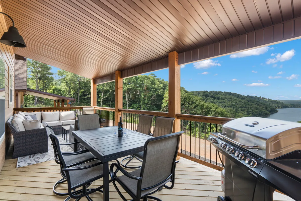 A spacious wooden deck with an outdoor dining table and comfortable seating area overlooks Table Rock Lake. The setting is tranquil, with a scenic view of the lake stretching into the distance, inviting guests to relax, dine, or sip morning coffee while enjoying the serenity and privacy of the deck.