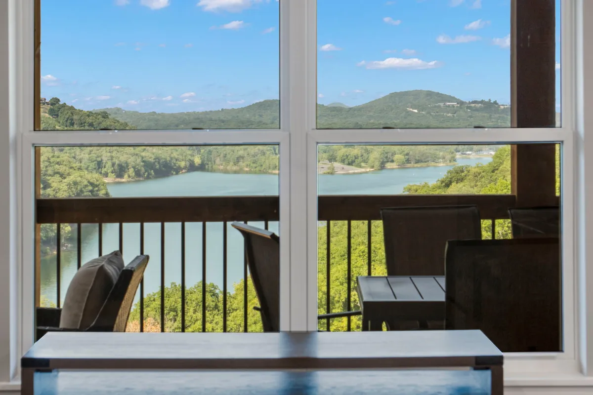 The image showcases a tranquil balcony overlooking Table Rock Lake, with cozy outdoor furniture perfectly positioned to take in sweeping water and mountain views. The scene captures the magic of a misty morning or golden sunset, inviting guests to relax, dine, or stargaze while surrounded by natural Ozark beauty.