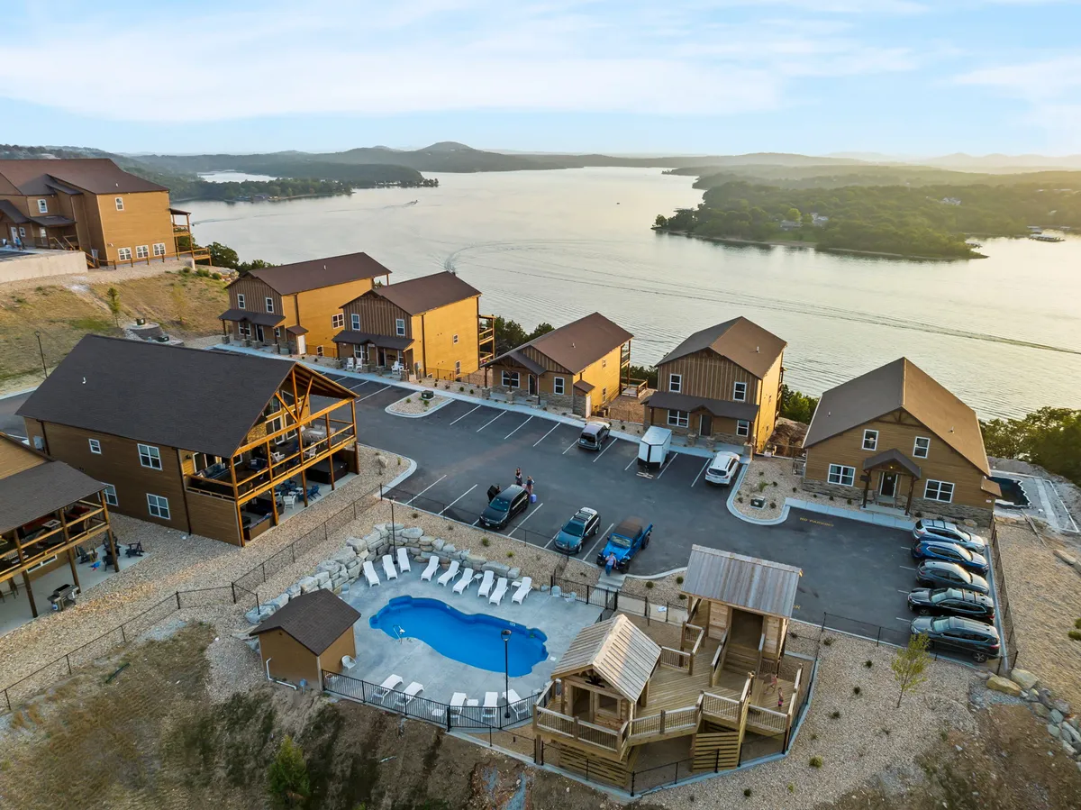 A vibrant scene with a lakeview swimming pool, a playful playground structure, and wooden cabins in the background. The pool area is lively, family-friendly, and ideal for both recreation and relaxation, demonstrating access to pools and a treehouse playground as described in the section.